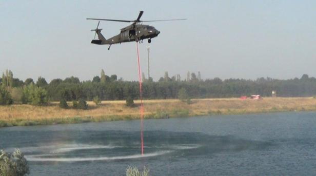 Ein Hubschrauber befüllt einen See mit Wasser, möglicherweise zur Brandbekämpfung.