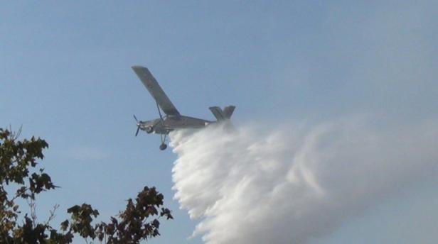 Ein Löschflugzeug setzt Wasser über einem Waldgebiet ab.