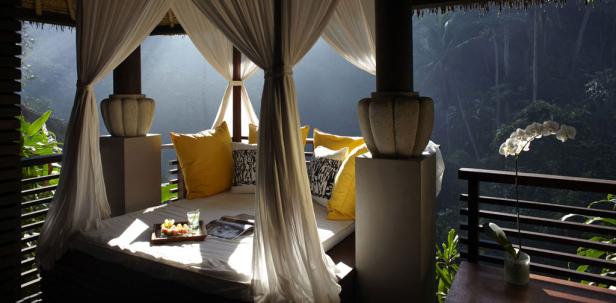Ein Himmelbett mit gelben Kissen auf einer Terrasse mit Blick auf einen tropischen Wald.