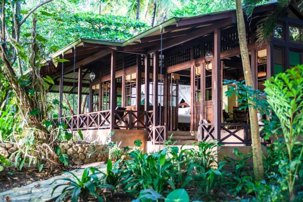 Ein Holzhaus mit Veranda inmitten üppiger tropischer Vegetation.