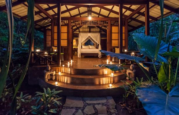 Ein offener Pavillon mit einem Himmelbett, beleuchtet mit Kerzen in einem tropischen Garten.