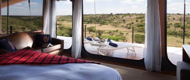 Blick aus einem luxuriösen Zelt auf die afrikanische Savanne mit Liegestühlen auf einer Holzterrasse.