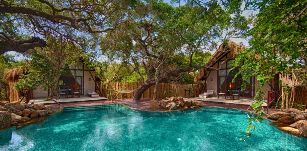 Ein tropischer Poolbereich mit strohgedeckten Hütten und üppiger Vegetation.