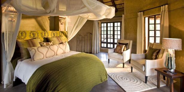 Ein Schlafzimmer mit Himmelbett, zwei Sesseln und einem Teppich mit konzentrischen Kreisen.