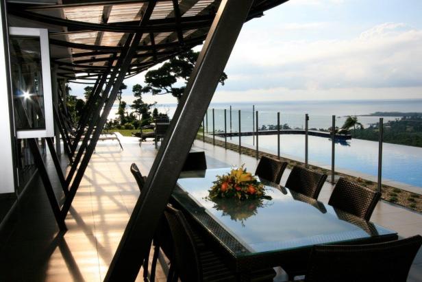 Ein Esstisch mit Blumen steht auf einer Terrasse mit Blick auf einen Pool und das Meer.
