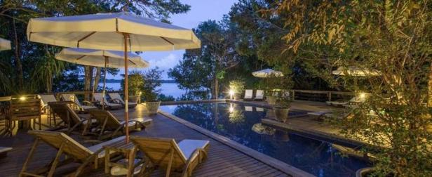Ein Swimmingpool mit Liegestühlen und Sonnenschirmen in einem Resort am Abend.
