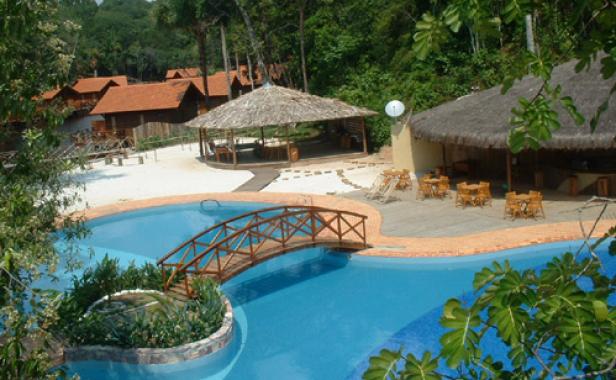 Ein Resort mit strohgedeckten Hütten und einem Pool mit einer kleinen Holzbrücke.