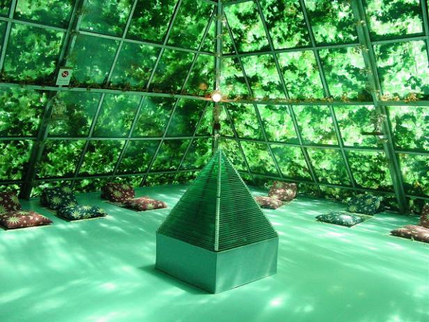 Ein pyramidenförmiger Raum mit Kissen und Glaswänden, die mit Grünzeug bedeckt sind.