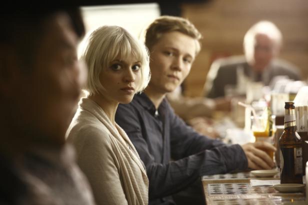 Eine junge Frau mit blonden Haaren sitzt mit einem jungen Mann an einem Tisch in einem Restaurant.