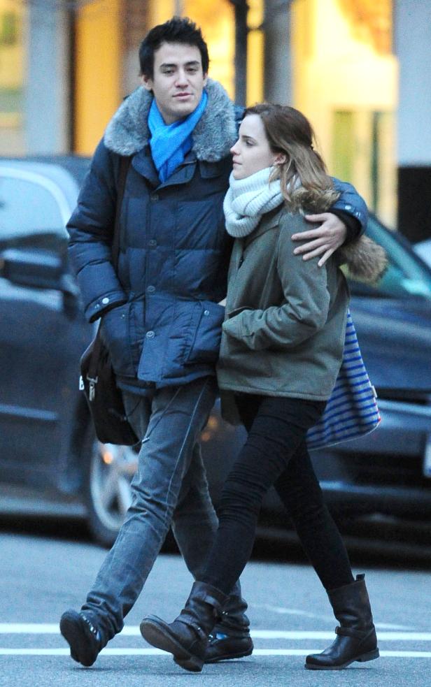 Emma Watson wird von einem Mann mit blauem Schal umarmt, während sie eine Straße entlanggehen.