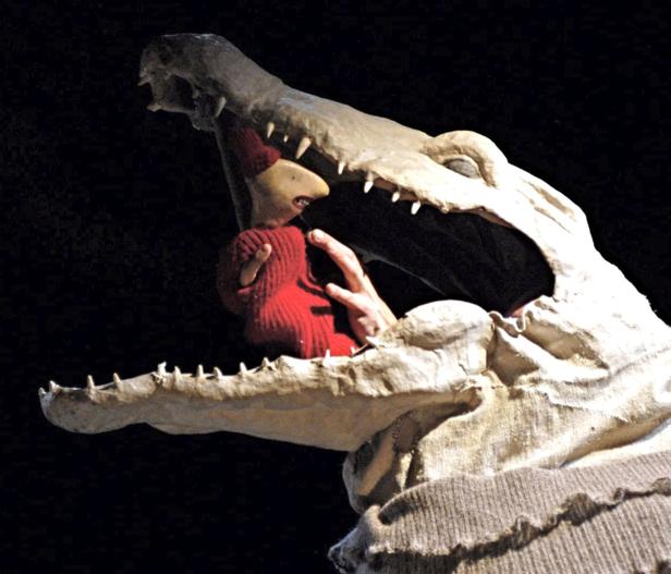 Eine Puppe wird von einem Krokodil mit großen Zähnen gefressen.