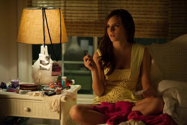 Emma Watson sitzt in einem gelben Kleid auf einem Bett und hält eine Zigarette in der Hand.