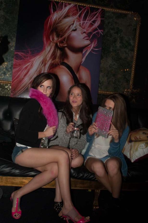 Drei junge Frauen sitzen auf einem Sofa vor einem großen Poster.