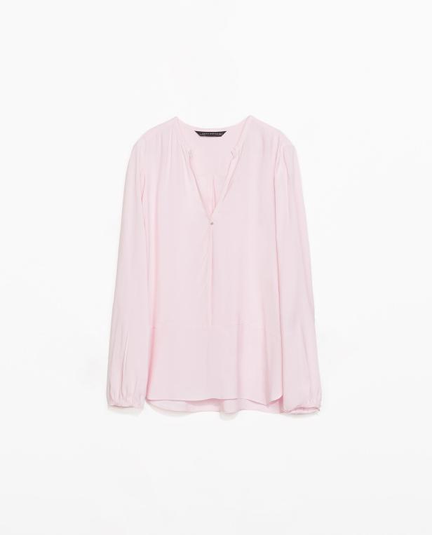 Eine hellrosa, langärmlige Bluse vor einem weißen Hintergrund.