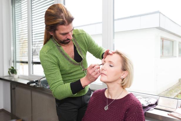 Ein Visagist trägt Make-up auf das Gesicht einer Frau auf.