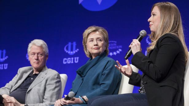 Bill Clinton, Hillary Clinton und Chelsea Clinton sitzen auf einer Bühne.