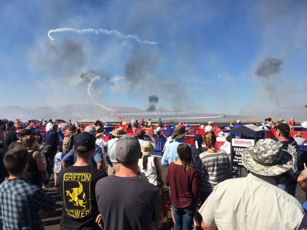 Eine Menschenmenge beobachtet eine Flugshow mit Rauchspuren am Himmel.
