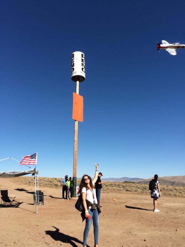 Eine Frau posiert vor einem Flugzeug und einem Schild mit der Aufschrift „Reno Air Races“.