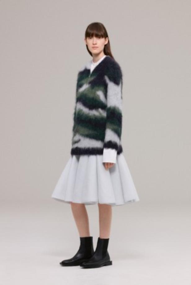 Eine Frau trägt einen gestreiften Pullover, einen weißen Rock und schwarze Stiefel.