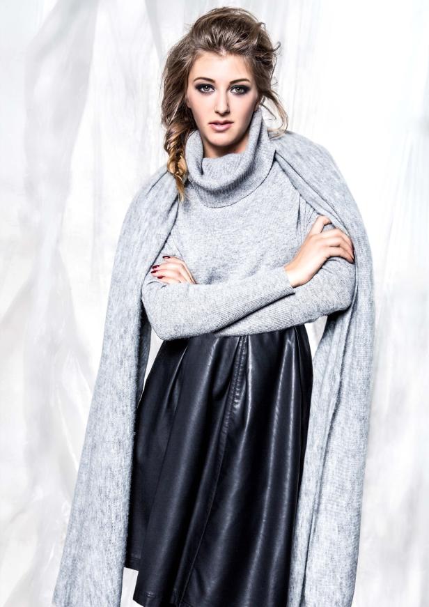 Eine Frau mit geflochtenem Haar trägt einen grauen Rollkragenpullover und einen schwarzen Lederrock.