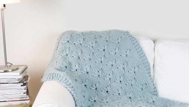 Eine hellblaue Strickdecke liegt auf einem weißen Sofa.