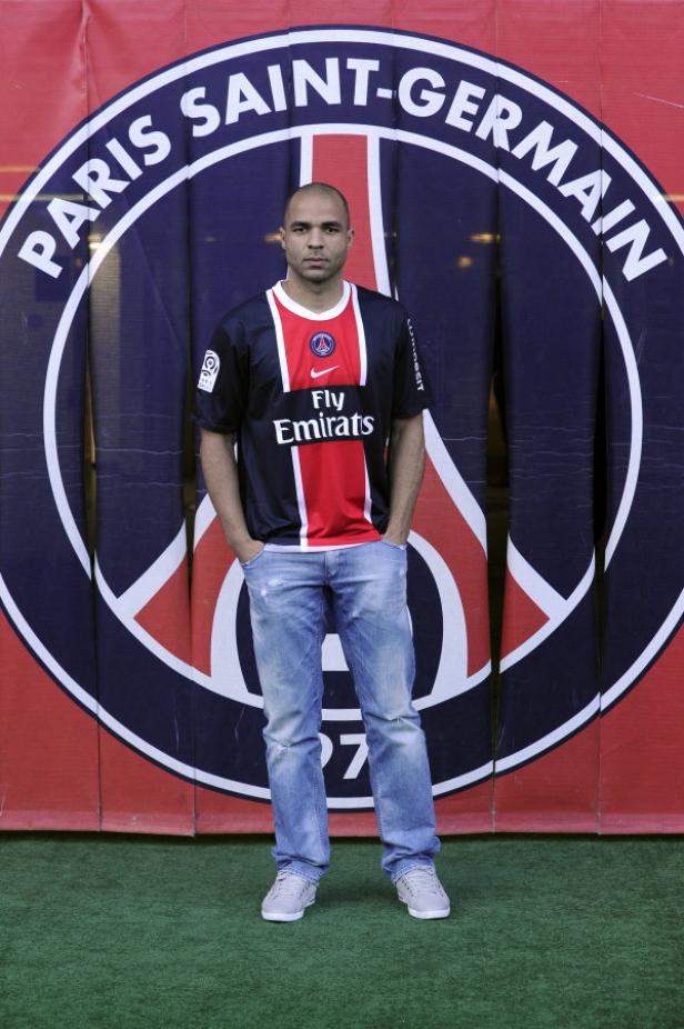 Ein Mann posiert vor dem Logo von Paris Saint-Germain.