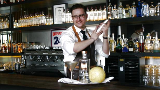 Ein Barkeeper mixt einen Cocktail hinter einer Bar mit vielen Spirituosenflaschen.