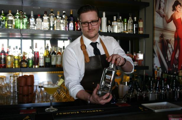 Ein Barkeeper mit Brille hält eine Flasche Absolut Elyx in einer Bar.