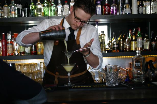 Ein Barkeeper mixt einen Cocktail hinter einer Bar mit vielen Spirituosenflaschen.