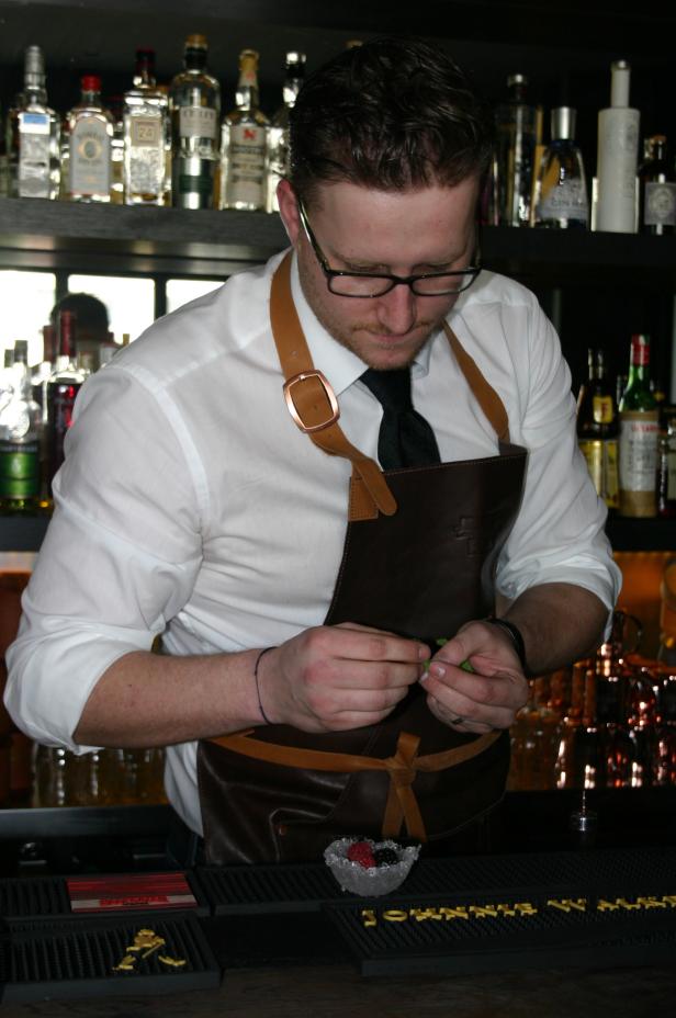 Ein Barkeeper bereitet einen Cocktail mit Minze vor einer Bar zu.