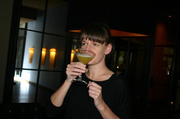 Eine Frau mit braunen Haaren trinkt einen Cocktail aus einem Martiniglas.