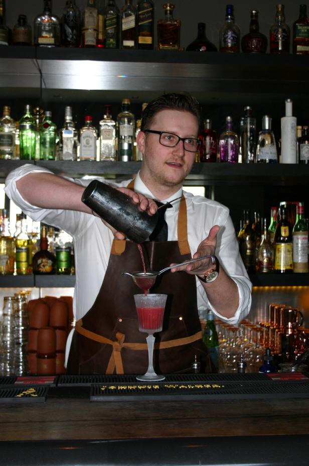 Ein Barkeeper mixt einen roten Cocktail in einer Bar.