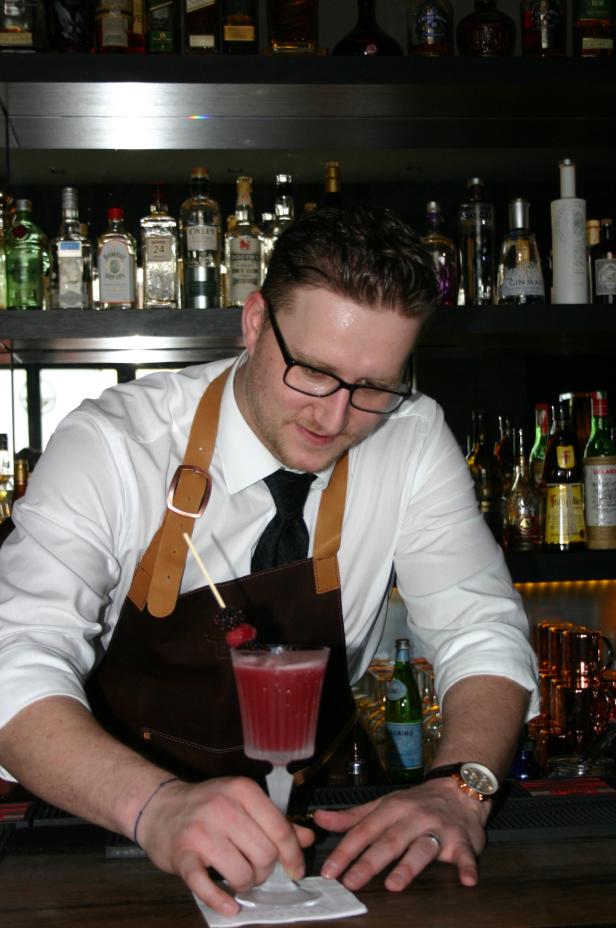 Ein Barkeeper bereitet einen Cocktail mit Beeren in einer Bar zu.