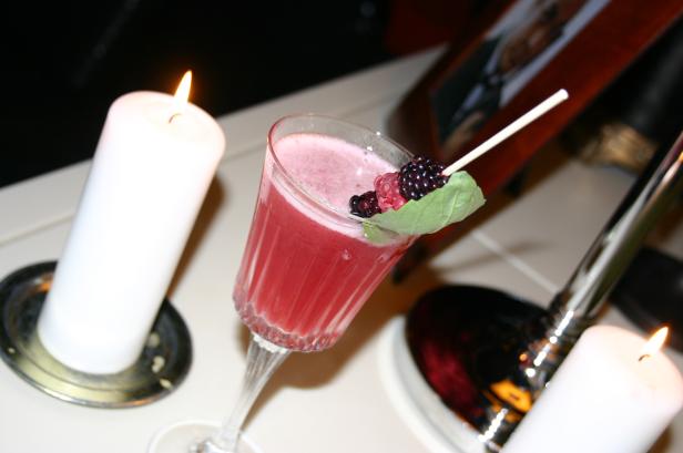 Ein Cocktail mit Beeren garniert, umgeben von brennenden Kerzen.