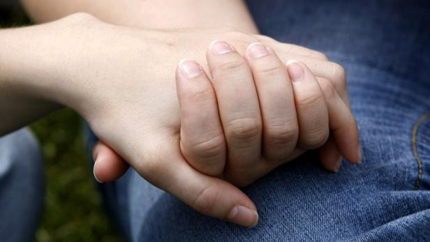 Eine Hand liegt auf dem Schoß einer Person in Jeans.