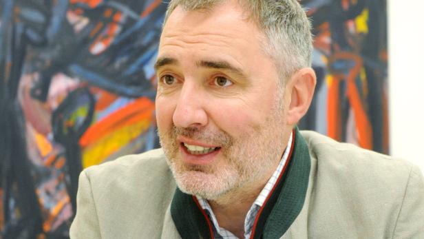 Ein Mann mit Bart und Jackett vor einem abstrakten Gemälde.