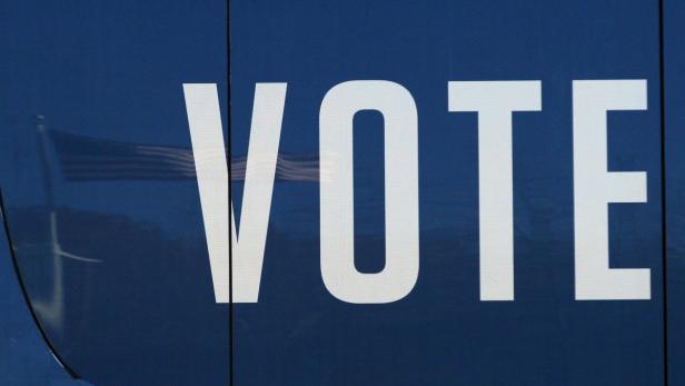 Das Wort „VOTE“ (Wählen) vor einer unscharfen amerikanischen Flagge.