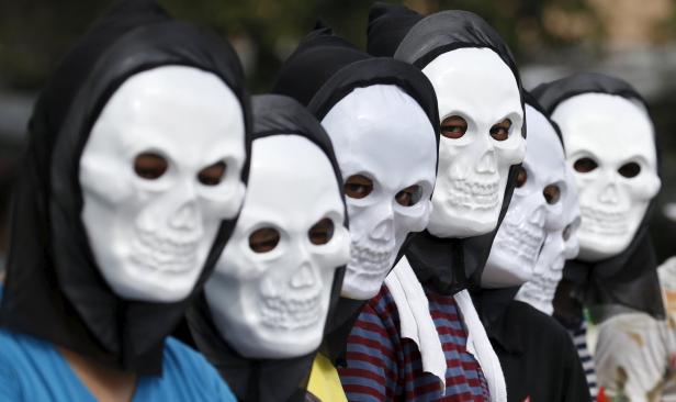 Eine Gruppe von Menschen trägt Totenkopfmasken und schwarze Kapuzen.