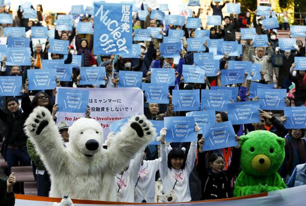 Menschen demonstrieren mit Schildern „Climate Action Now!“ und „Nuclear off!“ für den Klimaschutz.