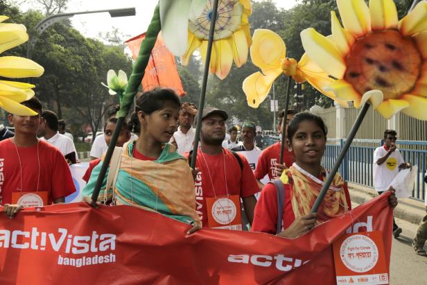 Menschen demonstrieren mit Sonnenblumen und einem Banner von „activista bangladesh“ für den Klimaschutz.