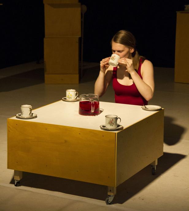 Eine Frau trinkt Tee an einem Tisch mit Teegeschirr.