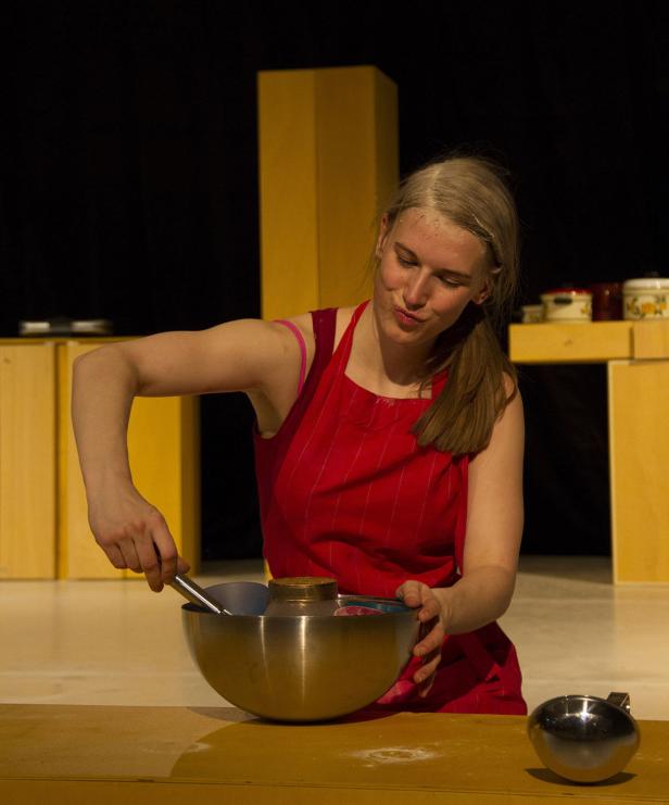 Eine junge Frau mit roter Schürze rührt Zutaten in einer Schüssel um.