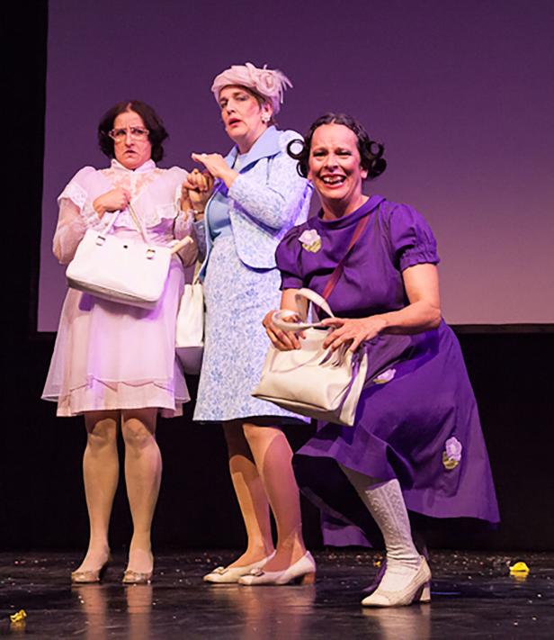 Drei Frauen in altmodischen Kleidern und Handtaschen stehen auf einer Bühne.