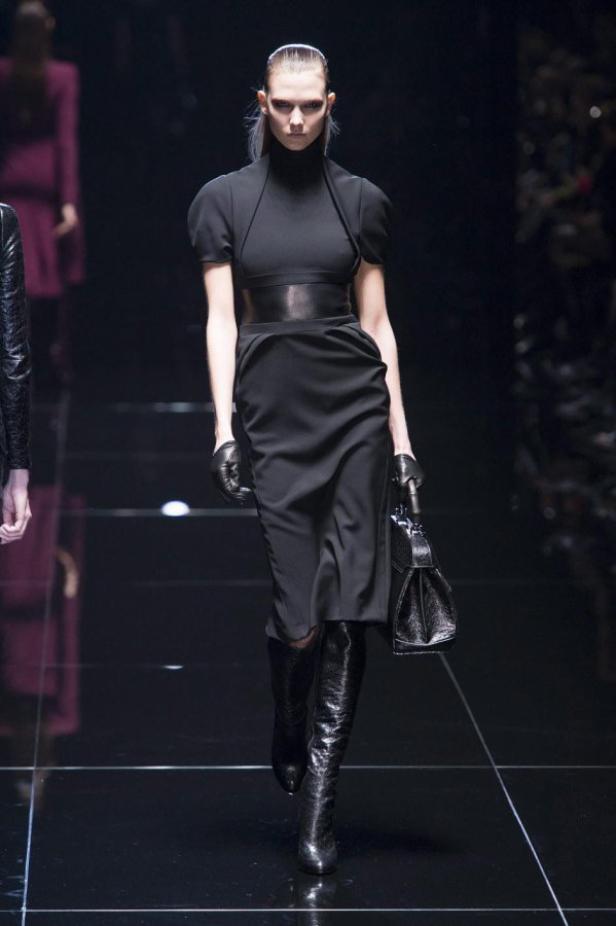 Eine Frau in einem schwarzen Kleid mit Gürtel und Stiefeln auf einem Laufsteg.