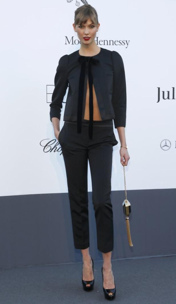 Karlie Kloss trägt ein schwarzes Hosen-Ensemble mit offenem Blazer und hält eine kleine goldene Handtasche.