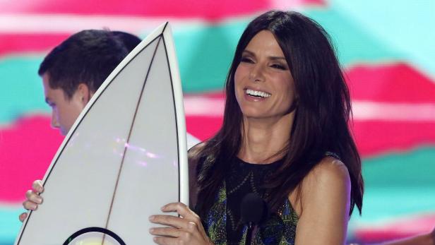 Sandra Bullock hält einen Preis in Form eines Surfbretts.