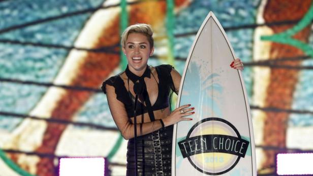 Miley Cyrus hält einen Teen Choice Award in Form eines Surfbretts.