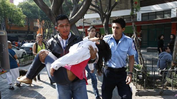 Ein Mann trägt eine bewusstlose Frau, während ein Sanitäter in der Nähe steht.