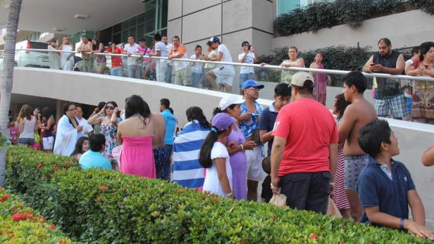 Eine Menschenmenge versammelt sich vor einem Gebäude, einige stehen auf einer erhöhten Plattform.