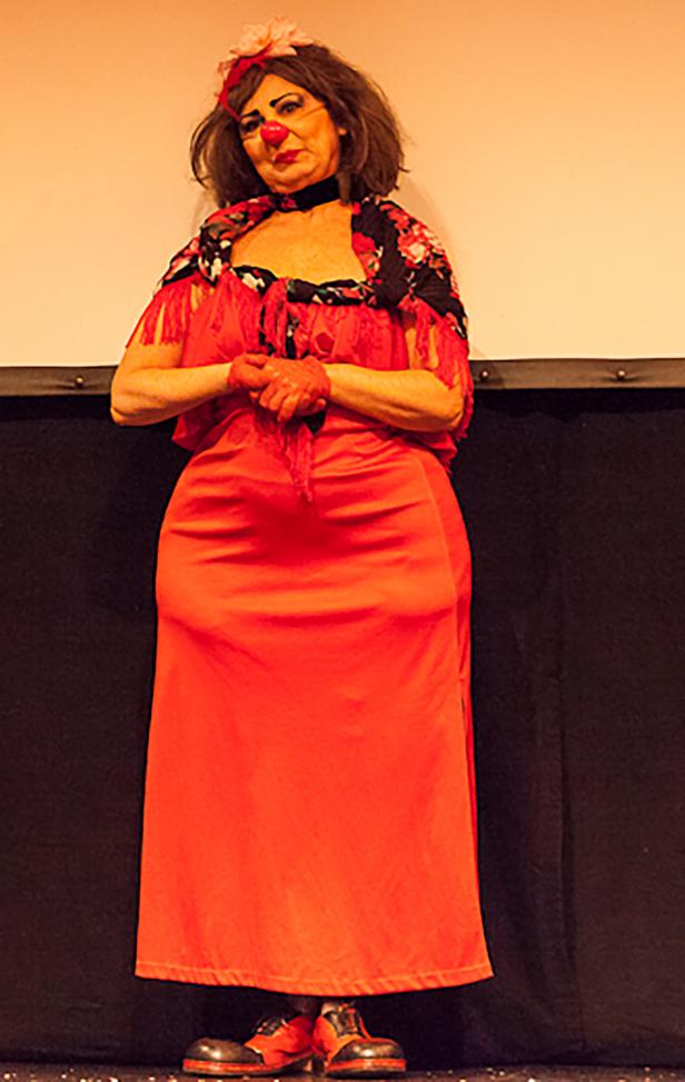 Eine Frau in einem roten Kleid und Clownschminke steht auf einer Bühne.